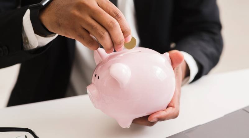 Man in suit putting coin into pink piggy bank